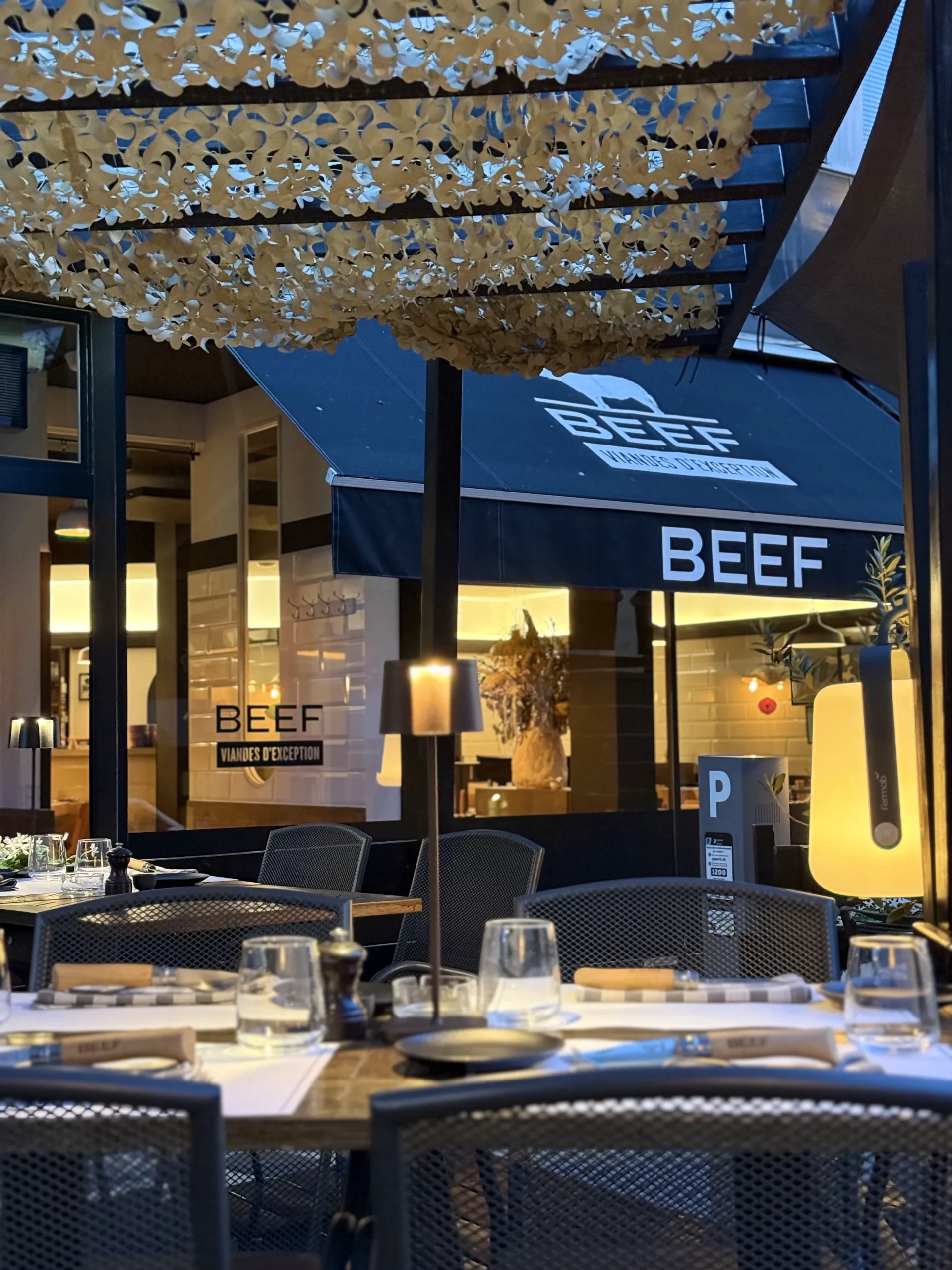 Terrasse couverte d’un restaurant avec tables dressées et enseigne BEEF visible en façade.