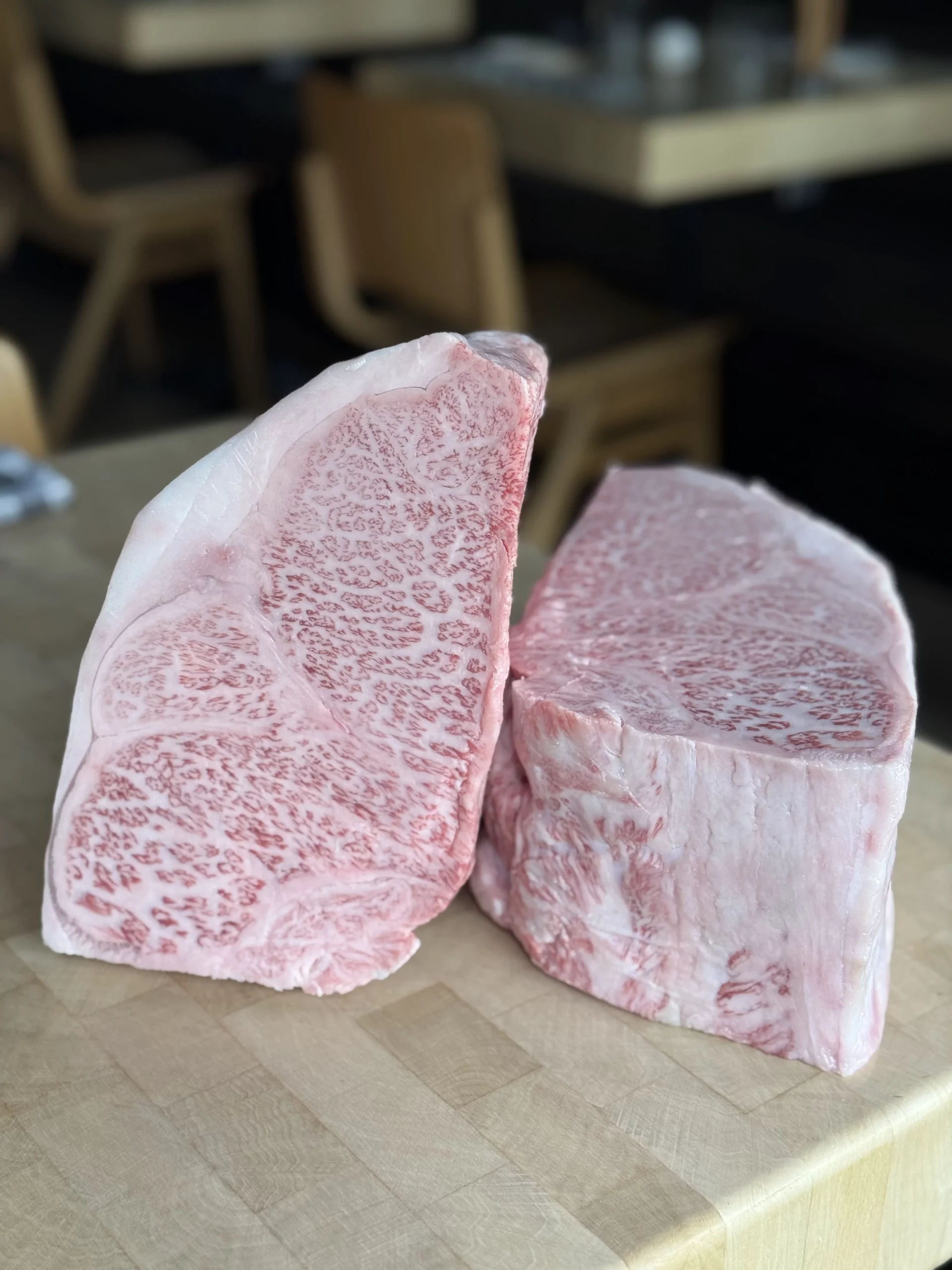 Deux steaks crus fortement persillés sont posés sur une planche claire, l’un appuyé contre l’autre.
