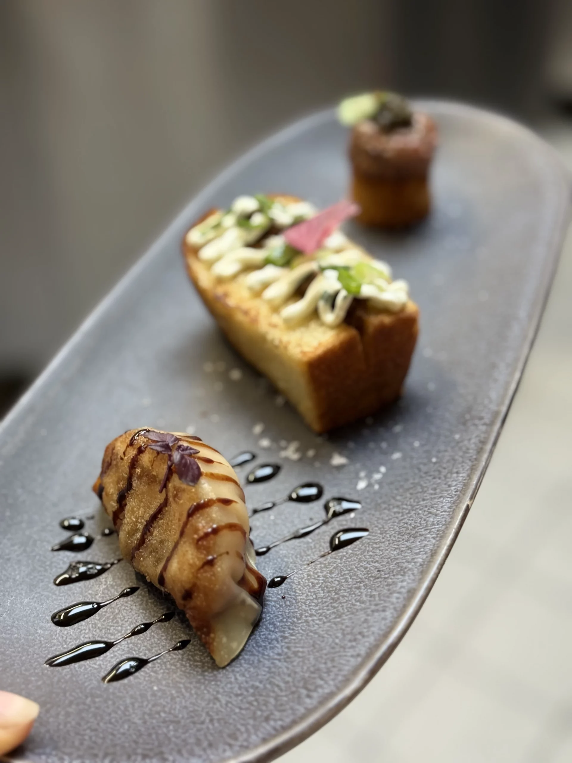 Petites assiettes dressées sur un plateau gris, avec une petite pièce brune pouvant évoquer un dessert à l’arrière