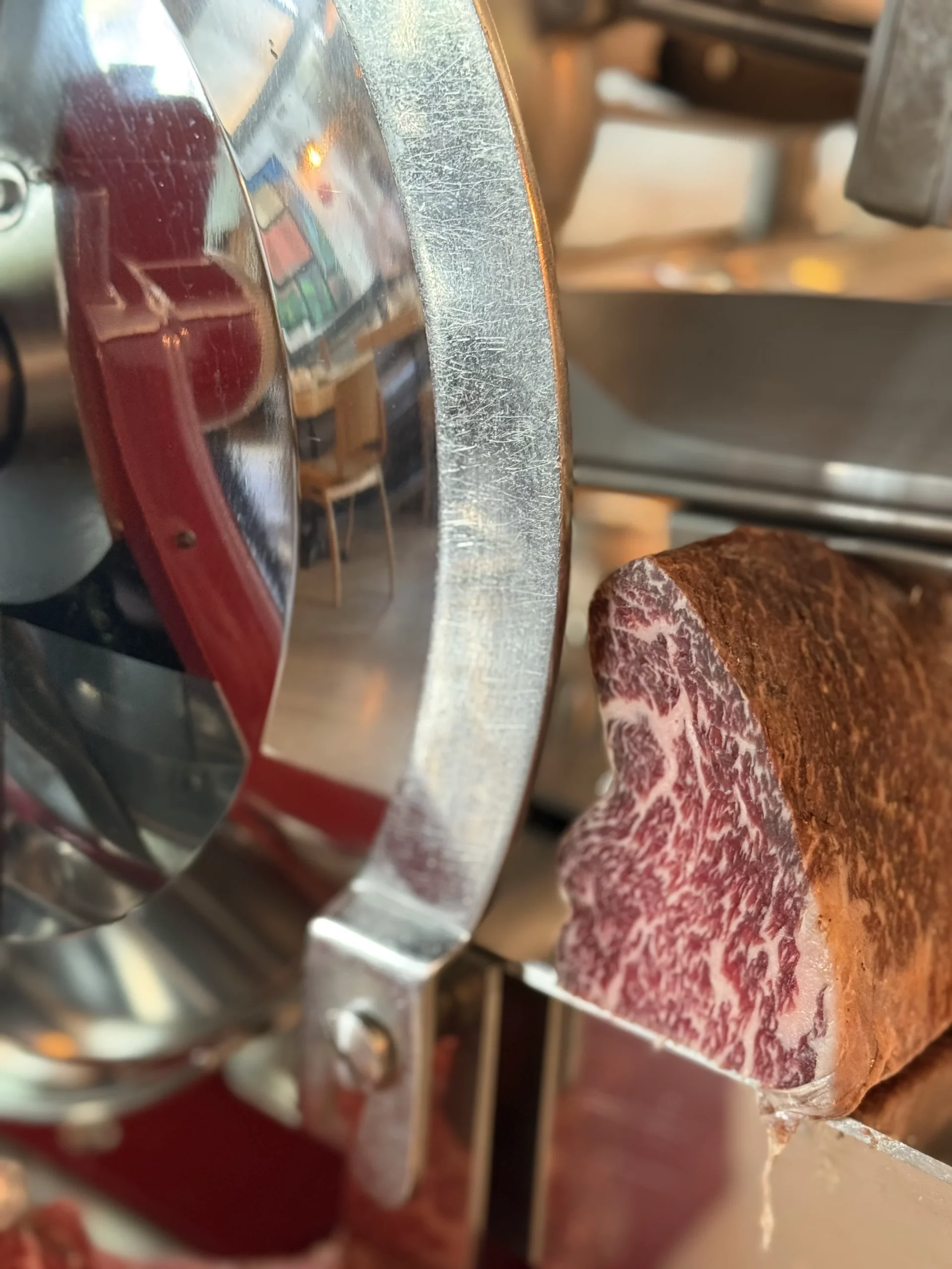 Un morceau de viande persillée est placé près d’une trancheuse métallique dans une cuisine commerciale.