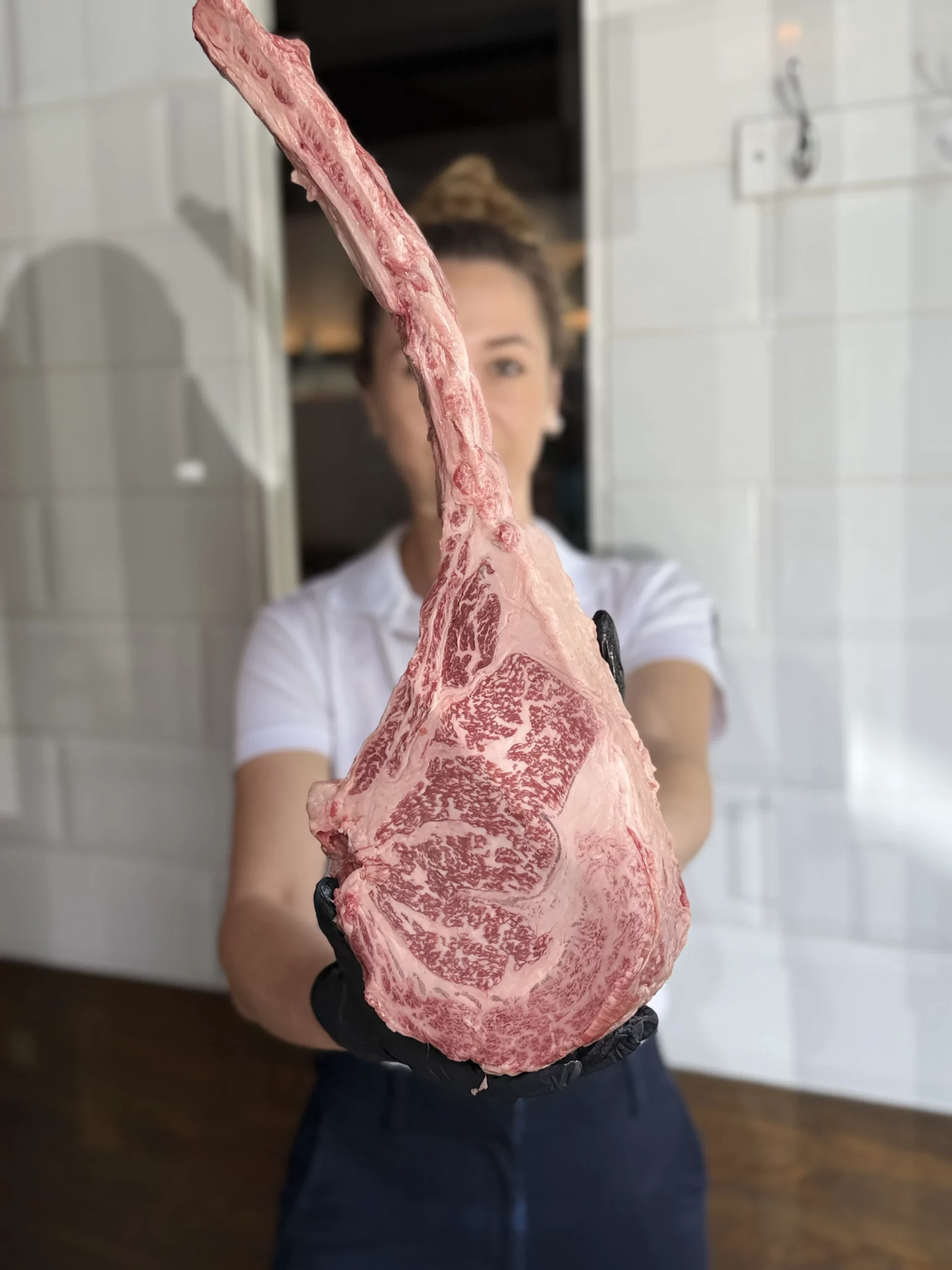 Une grande pièce de viande marbrée tenue par une personne gantée, dans une pièce carrelée.