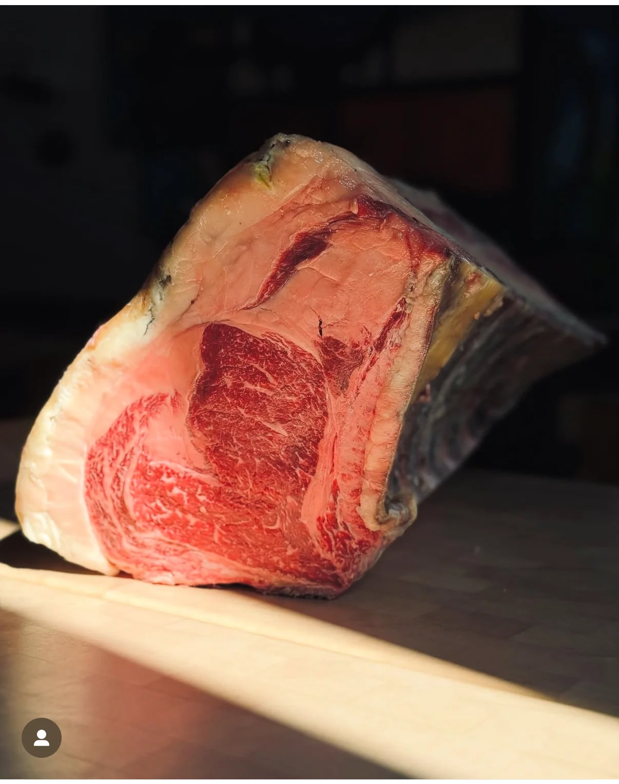 Morceau de bœuf cru avec marbrures et couche de gras posé sur une surface en bois.