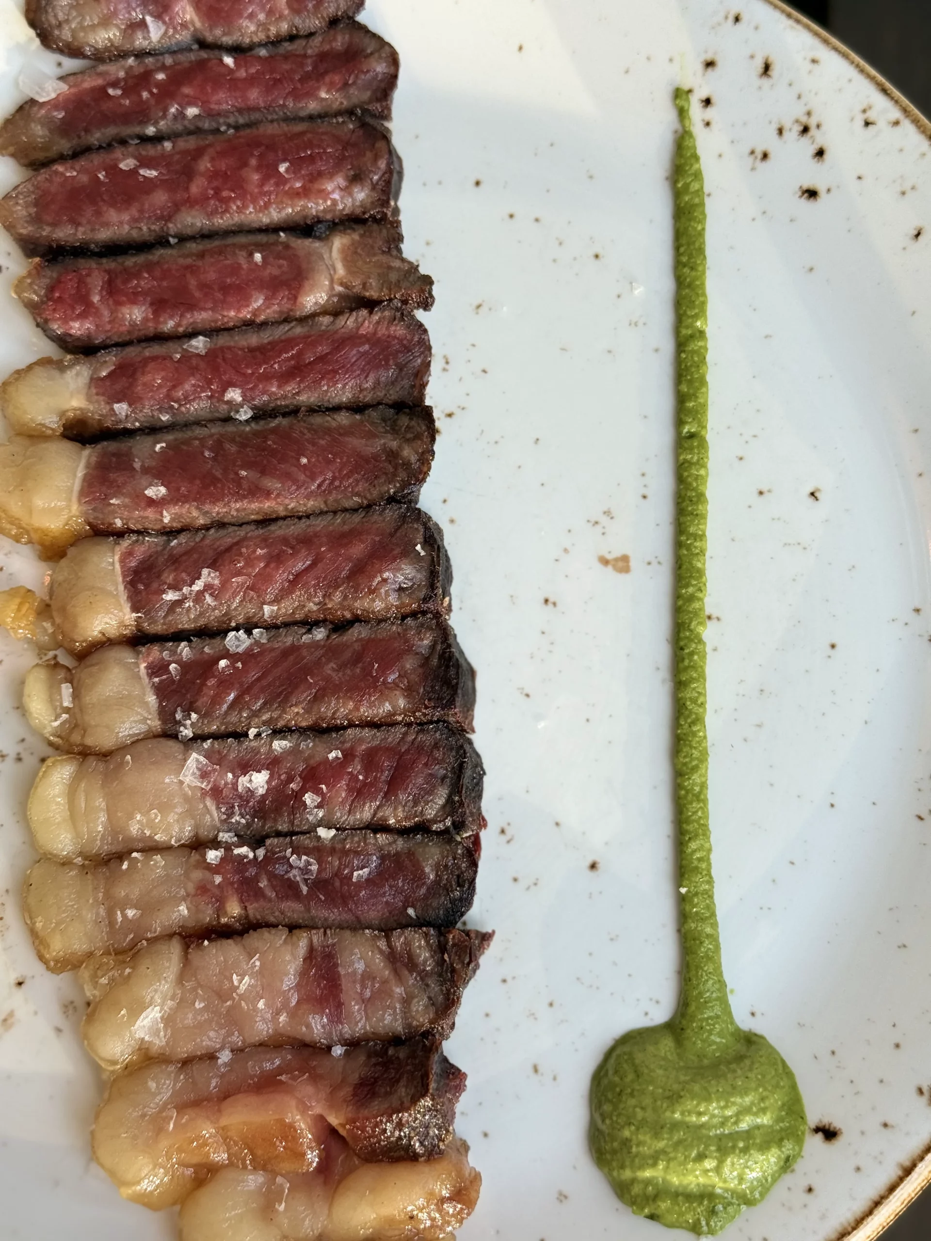 Tranches de viande saisies disposées sur une assiette blanche avec une sauce verte.