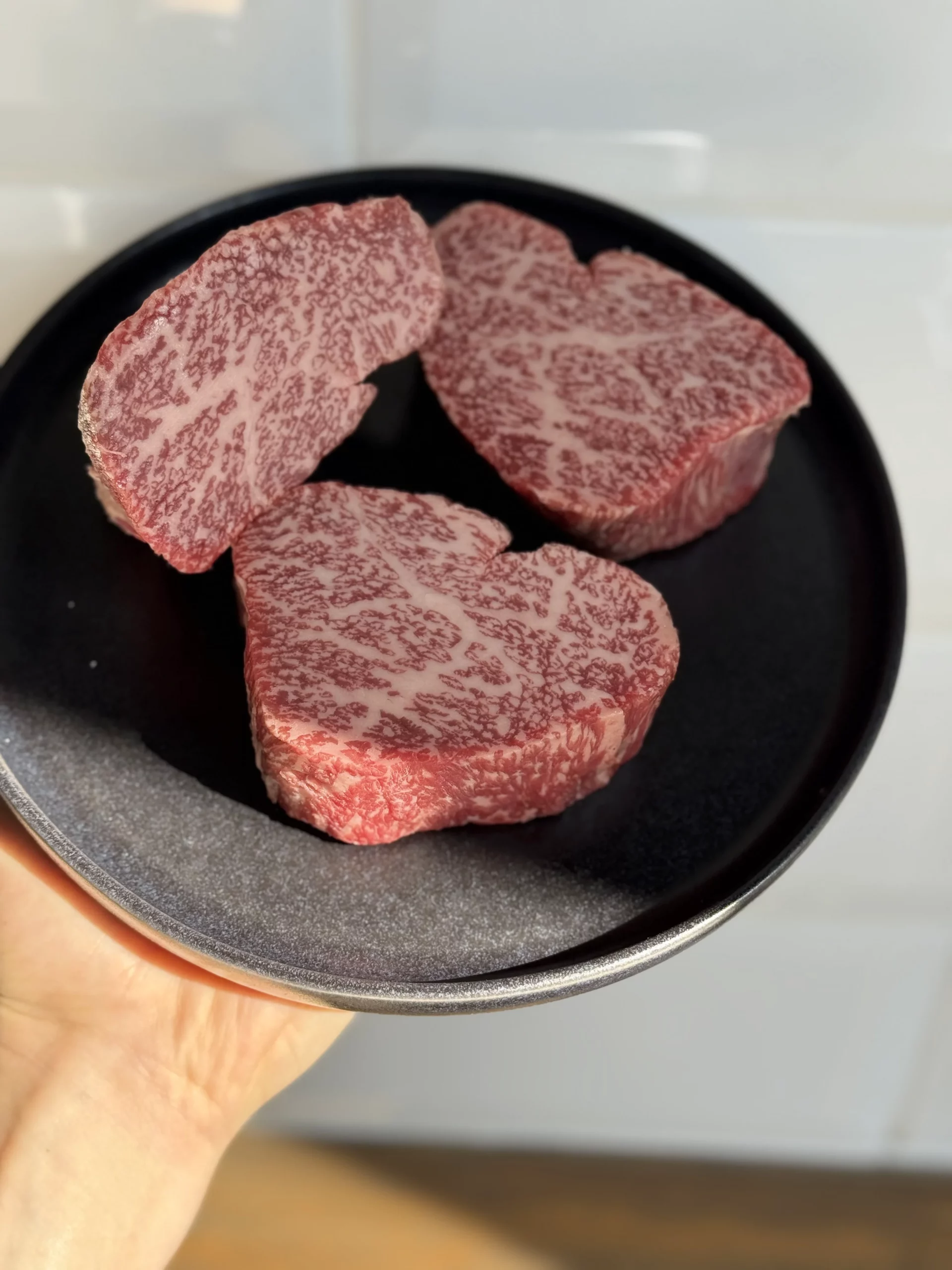 Trois steaks crus fortement persillés présentés sur une assiette noire.