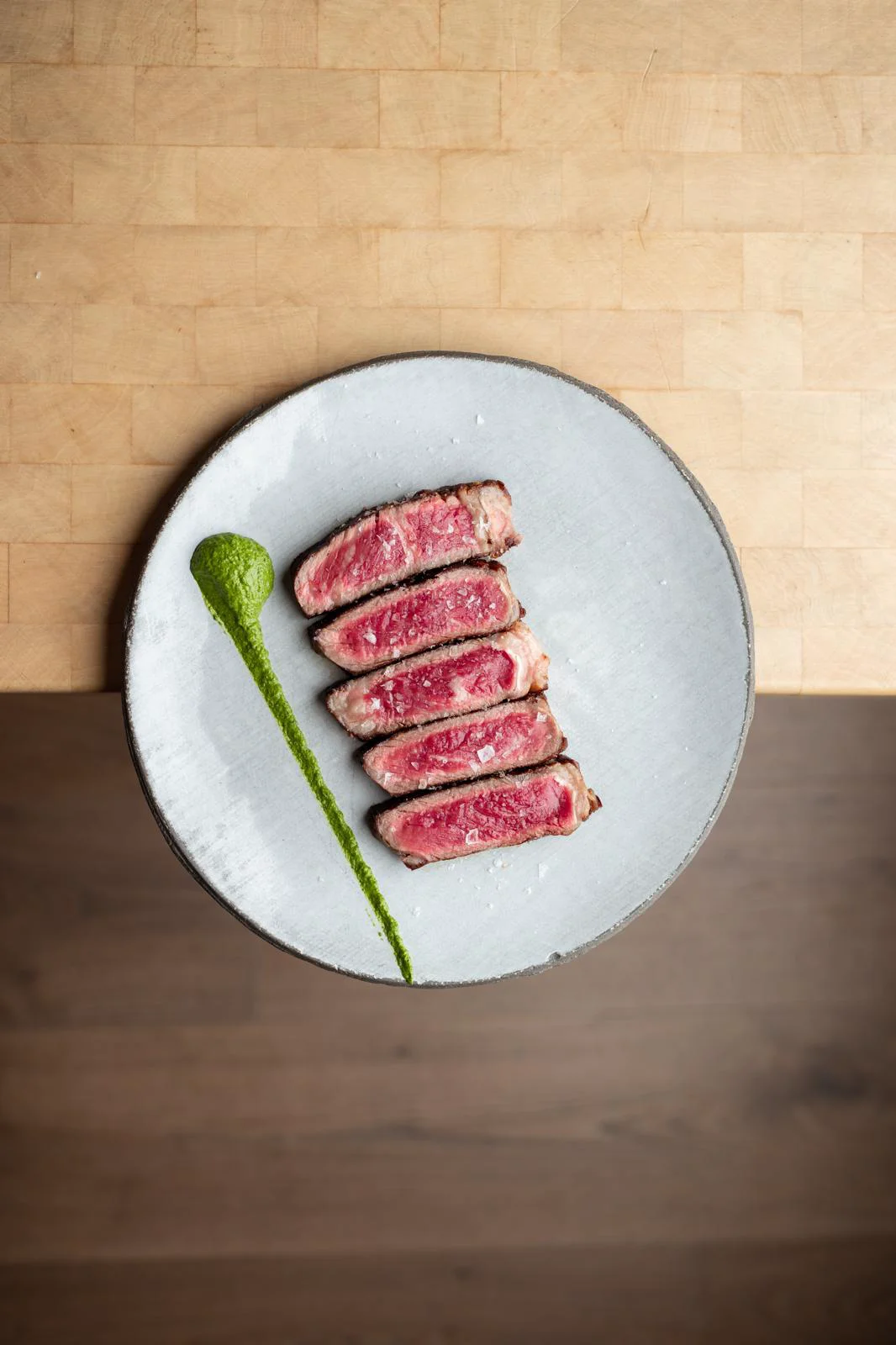 Tranches de viande cuite dressées avec une sauce verte sur une assiette.